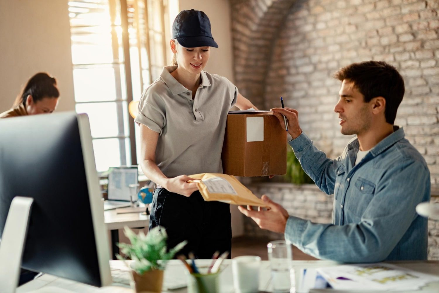 smiling-female-courier-delivering-package-businessman-while-he-is-working-office